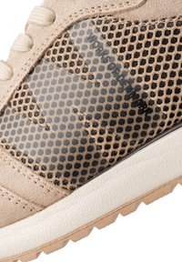 Basket à empeigne en daim beige et mesh, détails translucides, accents noirs, et semelle extérieure en caoutchouc blanc texturée avec motif antidérapant.