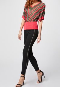 Monivärinen raitapaita vihreänä ja punaisena V-pääntiellä, yhdistettynä mustiin kapeisiin farkkuihin, joissa on sivuvetoketjut, ja mustiin korkokenkiin.