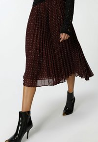 Jupe plissée bordeaux avec des pois bleu clair et une texture transparente, associée à des bottines en cuir noires avec des accents dorés.