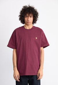 Burgundy cotton t-shirt with short sleeves, relaxed fit, and small gold logo accent on the chest. Smooth texture, crew neck design.