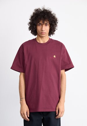 Burgundy cotton t-shirt with short sleeves, relaxed fit, and small gold logo accent on the chest. Smooth texture, crew neck design.