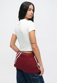 Λευκό κομμένο t-shirt με κοντά μανίκια που διαθέτει το μαύρο λογότυπο Jordan στην πλάτη. Φοριέται με μπορντώ σορτς που έχουν λευκές πλαϊνές ρίγες.