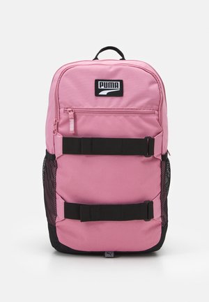Sac à dos Puma rose avec poche avant zippée, deux sangles noires horizontales, poches latérales en maille et poignée de transport sur le dessus.