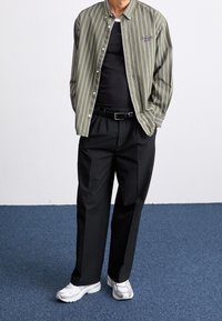 Knapp-up skjorta med olivgrön och vita ränder, kombinerad med högmidjade svarta byxor och vita sneakers. Enkel broderi detalj på skjortan.