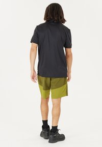 Mandligt atletisk sæt bestående af en sort kortærmet polo-shirt og olivengrønne shorts med farveblokdesign. Sorte sko fuldender looket.