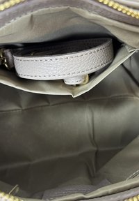 Vista interna di una borsa beige che mostra la fodera in tessuto, una tasca con cerniera e una tracolla di pelle avvolta con dettagli in oro.