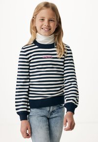 Pruhovaný svetr v námořnické modři a bílé barvě s vroubkovanými manžetami, na hrudi se pink logo "MCXX". Spárováno se světle modrými džíny.