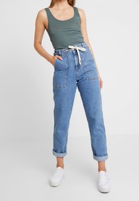 Top a righe verde abbinato a pantaloni in denim blu a vita alta con orli arrotolati e cintura con lacci bianchi. Sneakers bianche.