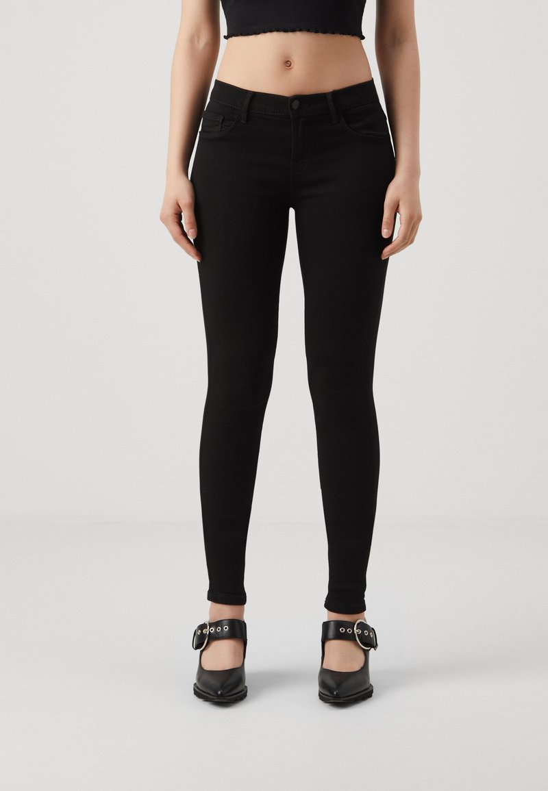 Jean skinny noir avec une texture lisse, taille mi-haute et design à cinq poches, associés à des talons noires à boucles.