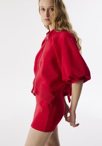 Rode ritsjack met oversized mouwen, gecombineerd met een bijpassende strakke rok. Glad materiaal, minimalistisch design, met zijzakken op de rok.