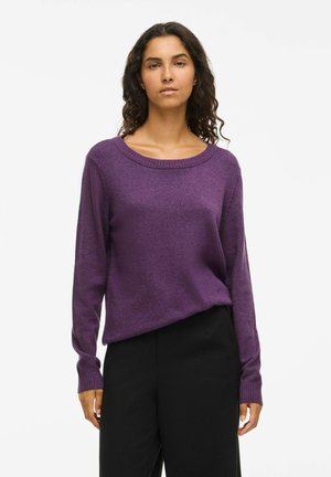 Suéter de punto morado con cuello redondo y mangas largas, que presenta puños acanalados y un corte relajado. Combinado con pantalones negros.