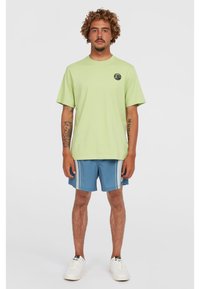 Camiseta de manga corta verde claro con cuello redondo y un logo circular. Combinada con pantalones cortos azules con rayas blancas y bolsillos laterales.