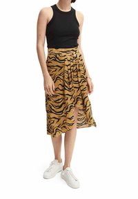 Tan midi rok met zwarte tijgerstrepen, voorzien van een wikkelontwerp en een split, gecombineerd met een aansluitend zwart tanktop en witte sneakers.
