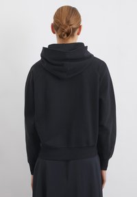 Felpa nera con cappuccio, dal fit rilassato, con polsini e orlo a coste, caratterizzata da una tasca kangaroo e una texture morbida. Vista dalla parte posteriore.