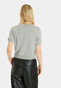 Szary sweter z krótkim rękawem o teksturowanej powierzchni, ozdobiony wypukłymi białymi i srebrnymi koralikami, zestawiony z czarnymi spodniami z sztucznej skóry.