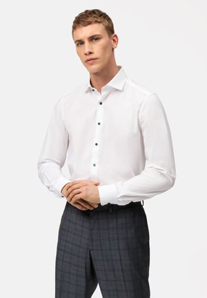 White dress shirt with a button-down collar, featuring dark buttons and long sleeves, paired with gray plaid trousers.