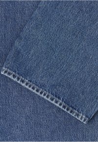 Gros plan sur un tissu en denim bleu montrant des coutures croisées et des surpiqûres détaillées sur des parties pliées.