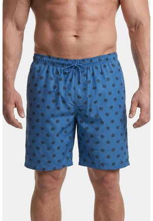 Mann trägt blaue Badeshorts mit schwarzen Sonnenmustern und einem Kordelzug in der Taille, gezeigt von der Taille bis zur Mitte des Oberschenkels vor weißem Hintergrund.