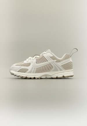Weißer und beiger Sportschuh zum Laufen mit Mesh-Einsätzen, Schnürverschluss, strukturierter Sohle und Zuglasche vor neutralem Hintergrund.