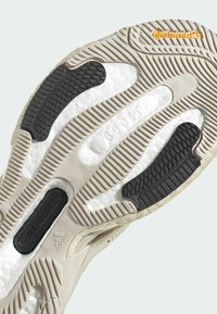 Sole tenisky Adidas s kombinací béžové a černé gumy, strukturovanými vzory a výraznou bílou polstrovanou oblastí s detaily loga.