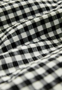 Crno-bijela gingham tkanina s kariranim uzorkom, koja prikazuje teksturiranu površinu i vidljive detalje šivanja.