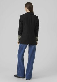 Blazer noir ajusté avec col cranté, associé à une chemise à rayures à manches longues et un jean bleu à jambes larges. Tissu lisse, design classique.