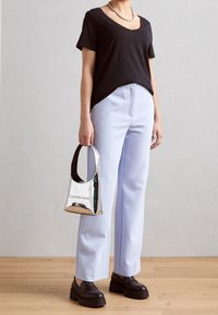 Osoba w czarnej koszulce z dekoltem w serek, jasnoniebieskich spodniach, czarnych, masywnych butach, trzymająca małą, metaliczno-srebrną torebkę Calvin Klein Jeans.