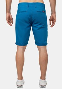Blauwe shorts met opgerolde pijpen, voorzien van dubbele achterzakken, contrasterende stiksels en een lichte stof. Klassiek casual ontwerp.