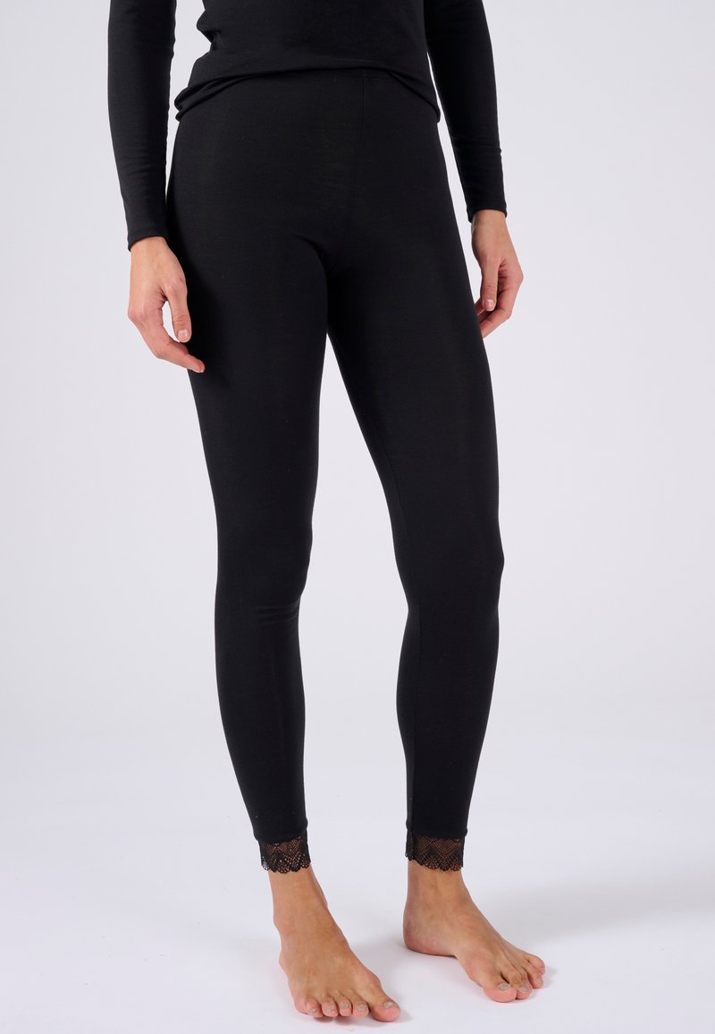 Leggings neri con una texture liscia e un design aderente. Il notevole orlo in pizzo alle caviglie aggiunge un tocco decorativo.
