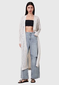 Cardigan leggero a trama aperta in crema con un design testurizzato, abbinato a jeans azzurri a vita alta e sandali neri.