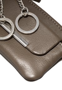 Borsa in pelle marrone con una texture liscia, dotata di una catena argentata e anelli portachiavi circolari, con un accento metallico etichettato "MAITRE."