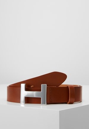 Bruine leren riem met een grote zilveren metalen H-vormige gesp, opgerold en weergegeven op een witte ondergrond tegen een effen achtergrond.