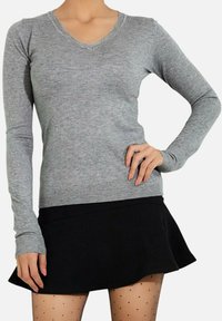 Pull gris à manches longues en V, fabriqué en tissu tricot doux, associé à une jupe noire évasée et des collants à pois. Texture lisse et design ajusté.