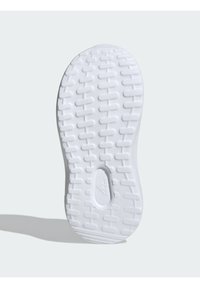 Bílá gumová podrážka tenisky se strukturovaným vzorem, obsahující žlábky a rýhy pro záběrové vlastnosti. Oválný výřez ve středu.