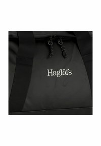 Zwarte sporttas van stevig materiaal, met een ritsluiting, dikke zwarte hengsels en een prominent weergegeven wit "Haglöfs" logo.
