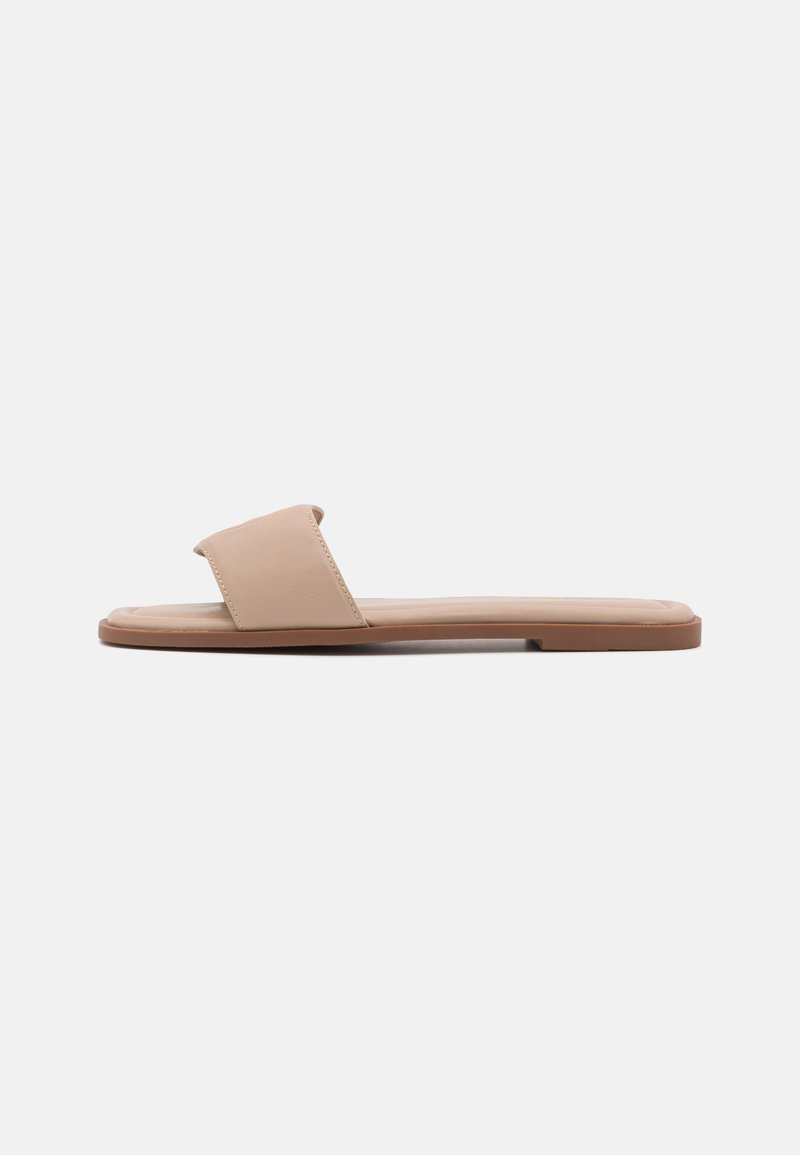 Beige flate sandaler med bredt rem og teksturert såle. Minimalistisk design med glatt overflate og lav profil. Ingen utsmykninger.
