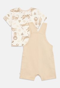 Camisa de manga corta color crema con estampados de animales y hojas en marrón claro, combinada con overoles beige que presentan dos bolsillos frontales y tirantes ajustables.