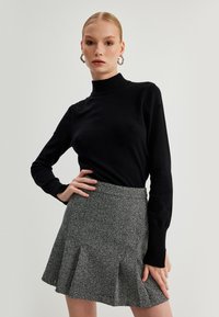 Suéter negro ajustado de cuello alto combinado con una falda acampanada gris que presenta un patrón texturizado y pliegues, mostrando un aspecto casual pero pulido.