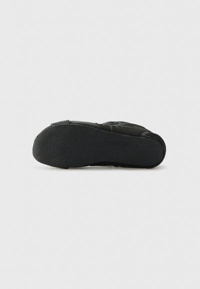 Semelle de sneaker noire en caoutchouc texturé, présentant une forme arrondie et un léger motif de semelle pour une meilleure adhérence. Le dessous est lisse et mat.