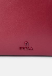 Rote Lederhandtasche mit strukturierten Oberflächen und eingeprägtem "FURLA"-Logo am Boden. Schlanke, rechteckige Form.
