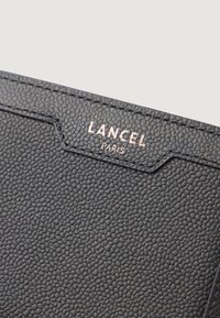 Czarny portfel z fakturowanej skóry z wytłoczonym logo „LANCEL PARIS” w różowym złocie. Posiada charakterystyczne krawędzie oraz wysublimowany wzór na powierzchni.
