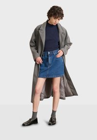 Abrigo de lana gris, suéter de canalé navy, falda mini de denim, zapatos negros, calcetines grises. El abrigo tiene un gran cuello; la falda presenta un cierre de botones en el frente.