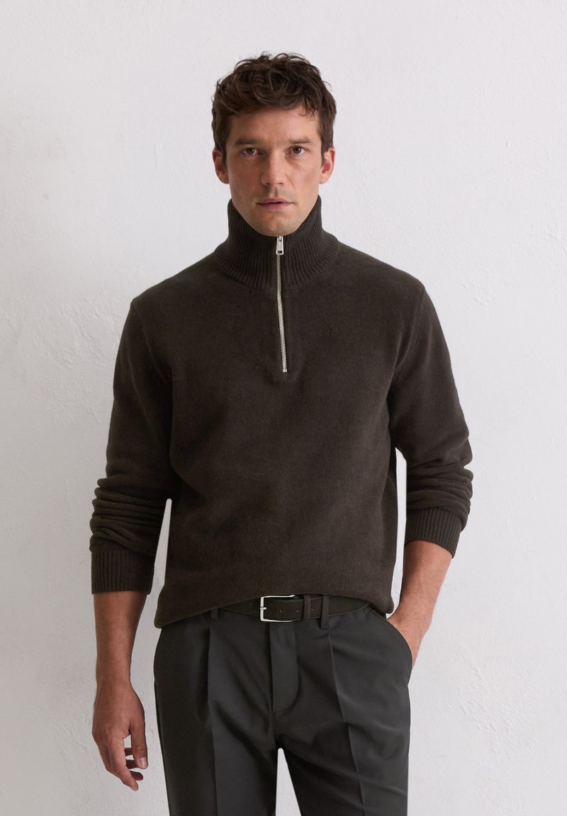 Dunkelbrauner Reißverschluss-Pullover mit geripptem Kragen und Bündchen, kombiniert mit schwarzen Hosen und einem Gürtel. Weicher Stoff, lässige Passform, schlichtes Design.