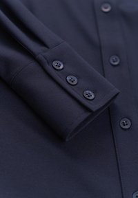 Marineblaue Knopfshirt-Manschette mit vier schwarzen Knöpfen, glatter Textur und leichtem Glanz, mit einem gefalteten Ärmel-Design.