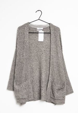Grijze grove gebreide cardigan met lange mouwen en twee zakken aan de voorkant, hangend aan een zwarte hanger tegen een witte achtergrond.