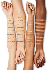 Échantillons de diverses teintes de peau sur quatre bras, montrant des nuances allant de claire à foncée, avec des étiquettes indiquant les noms et les tons de couleur spécifiques.