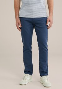 Chinos azul marino con corte ajustado, fabricados en algodón suave, y con bolsillos laterales, combinados con zapatillas blancas. Una camisa casual con estampado completa el look.