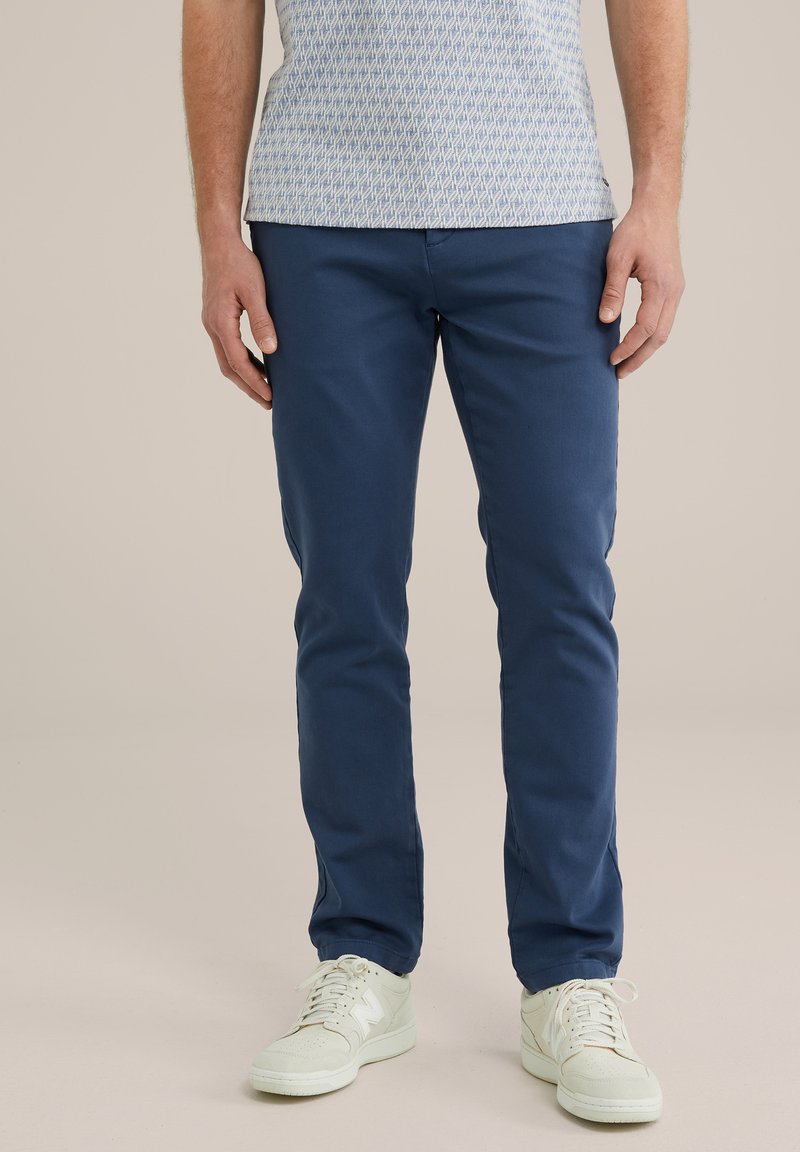Chinos azul marino con corte ajustado, fabricados en algodón suave, y con bolsillos laterales, combinados con zapatillas blancas. Una camisa casual con estampado completa el look.