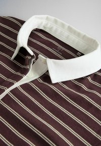 Bordeaux polo-shirt med hvide vandrette striber og hvid krave, lagt fladt med knaplukning og indvendig label synlig.