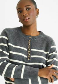 Gray striped sweater made of soft material, featuring a round neck, button placket with eight light brown buttons, and ribbed cuffs.